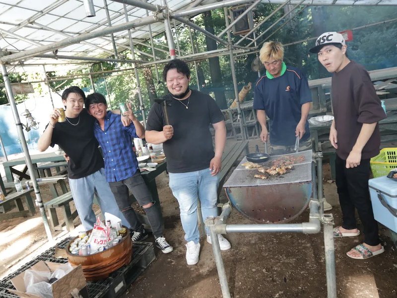 屋根付きのBBQエリアでドラム缶コンロを囲む5人